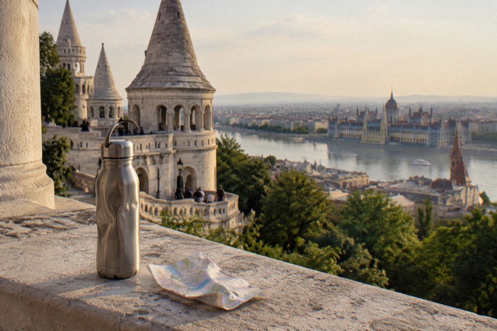 A reusable water bottle resting on a stone ledge above Budapest rooftops
