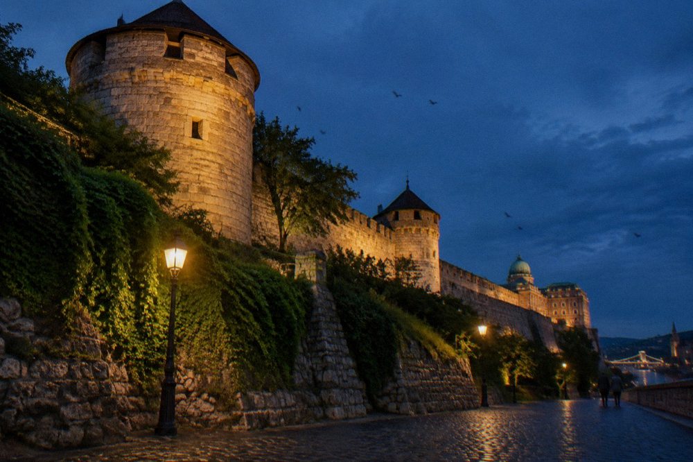 Lit walls and towers of Buda Castle Hill against a dark evening sky