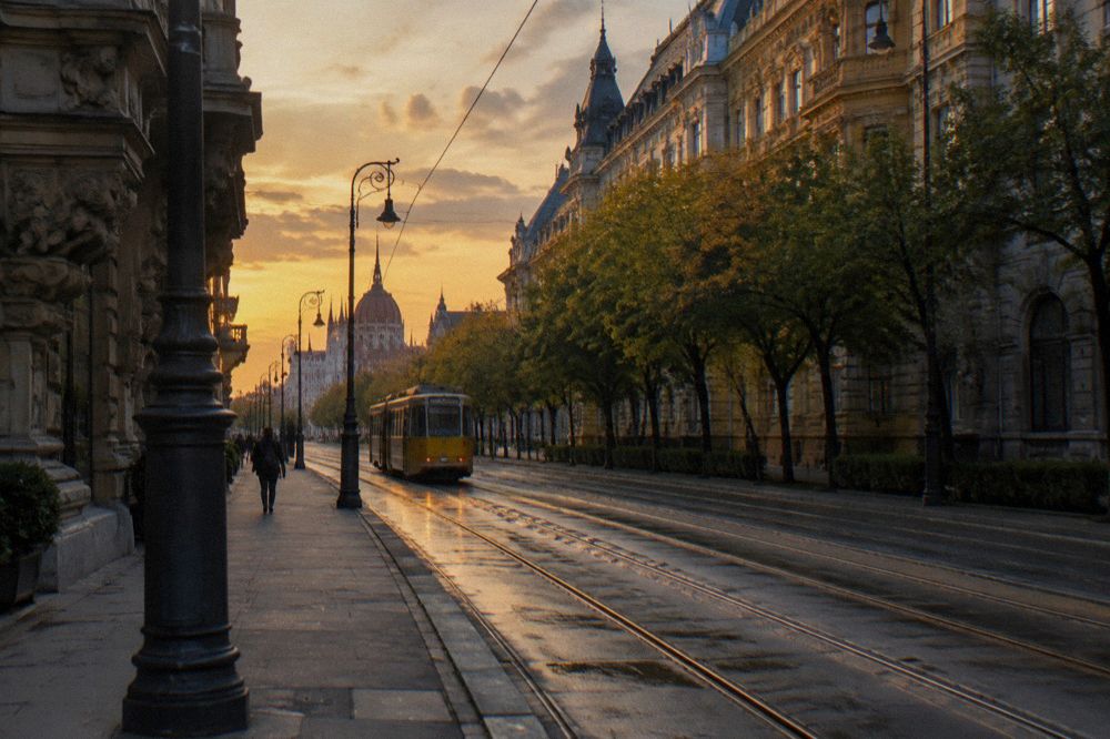 A Budapest street corner with a stone facade and tram tracks in the early evening