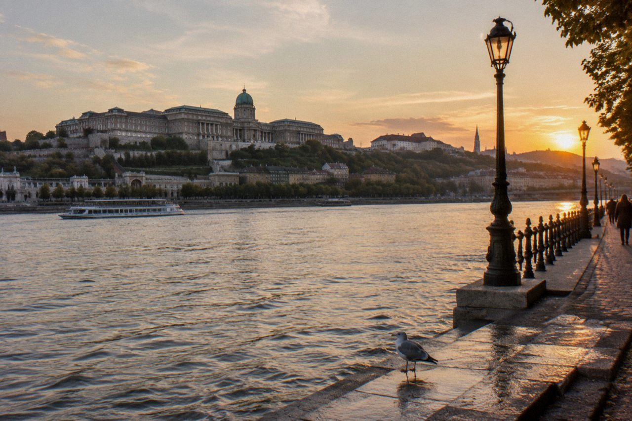 View across the Danube to Buda Castle Hill at golden hour, with the castle silhouette and riverfront buildings.
