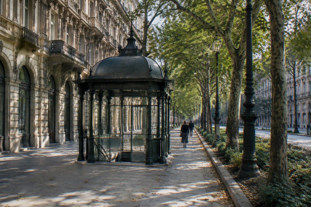 A small cast-iron metro pavilion on the tree-shaded pavement of Andrassy Avenue
