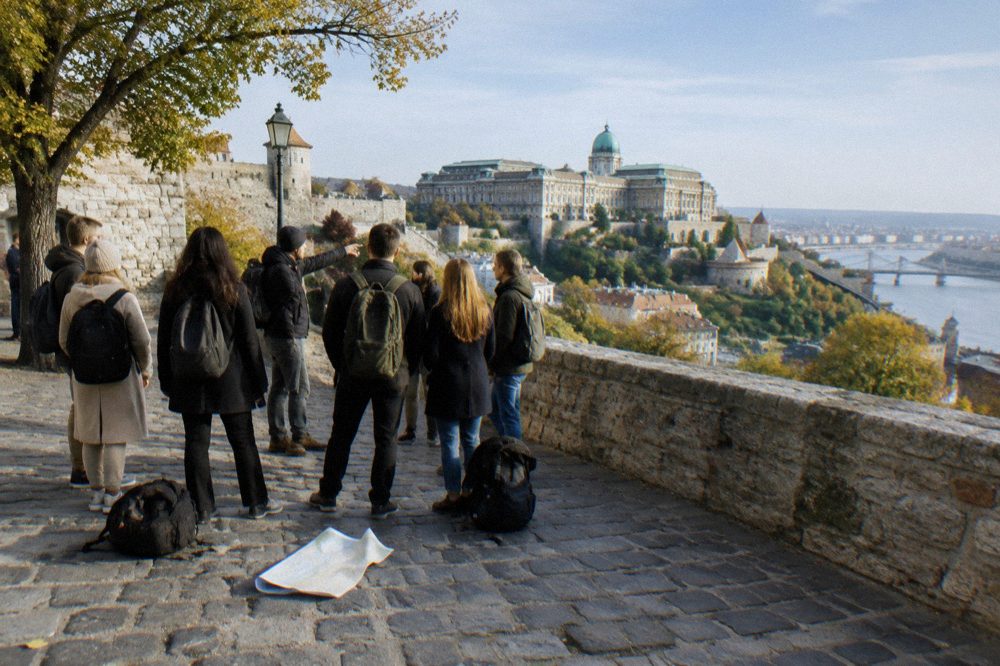 A free walking tour group gathered on the stone paving of a castle square in Budapest