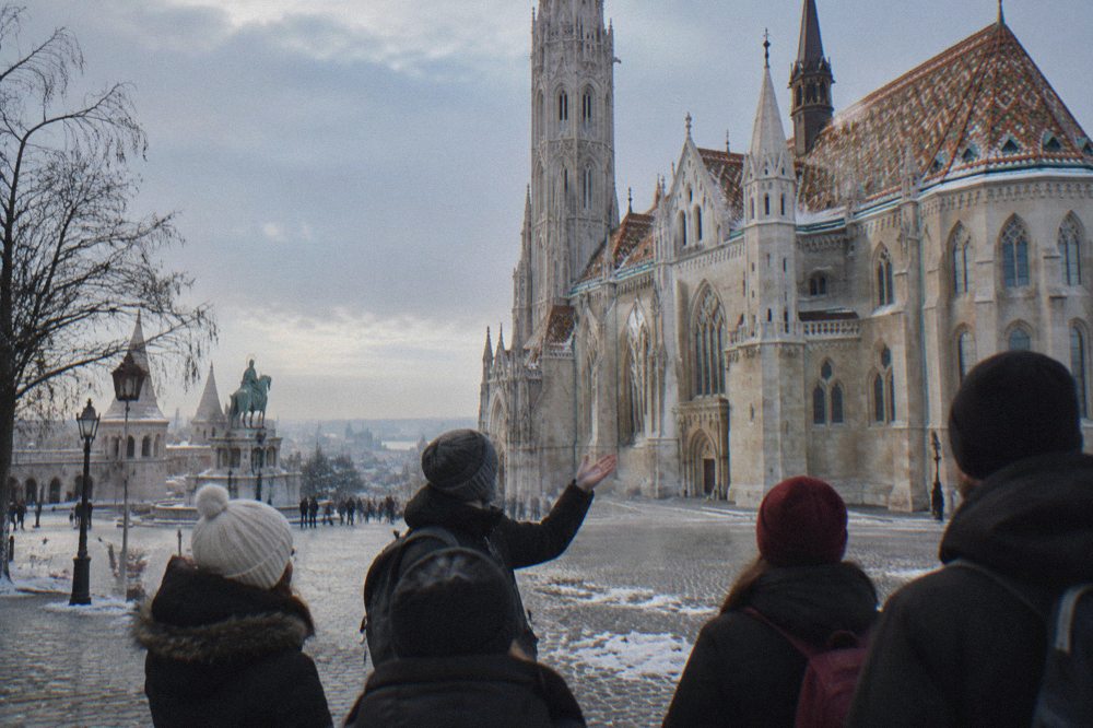 A local guide speaking to a small group of walkers on a snow-dusted square in central Budapest