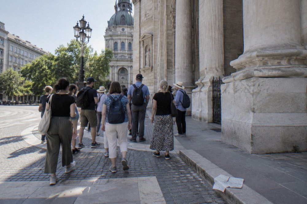 A gathering of walking tour participants beside a ornate city square at midday