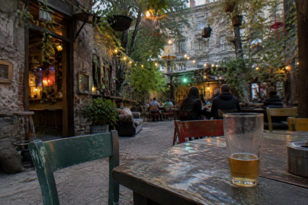 A warmly lit ruin bar courtyard with mismatched furniture and hanging plants