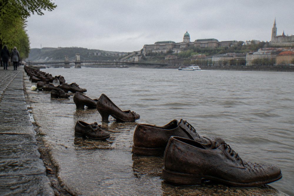 A row of cast iron shoes on a stone riverside promenade beside the Danube